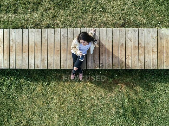 Молодая женщина сидит на деревянной набережной и проверяет свой смартфон — стоковое фото