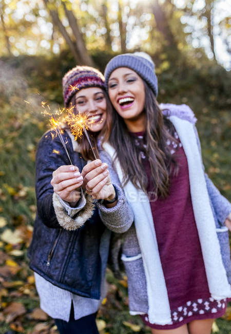 Dos mujeres felices sosteniendo bengalas en un bosque otoñal - foto de stock