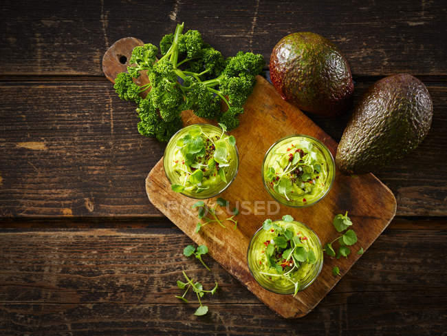 Glasses of avocado cream with chili flakes, cress and parsley — Stock Photo