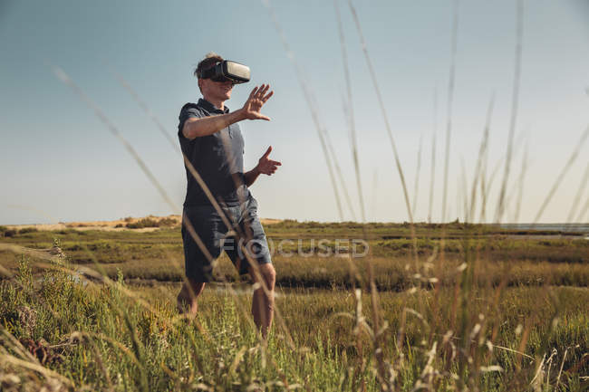 Mature man wearing VR glasses walking trough grass — Stock Photo