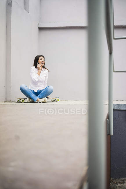 Сміється молода жінка по телефону сидить на скейтборді — стокове фото