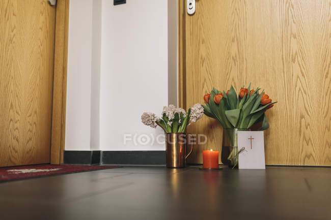 Flores de despedida, vela y tarjeta de condolencias en la puerta del apartamento del vecino fallecido - foto de stock