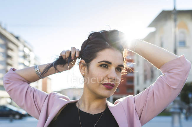 Молодая женщина регулирует свои волосы в городе — стоковое фото