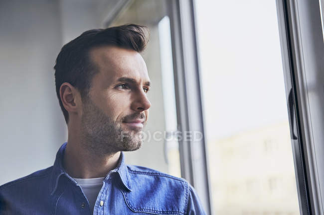 Retrato del hombre confiado mirando por la ventana - foto de stock