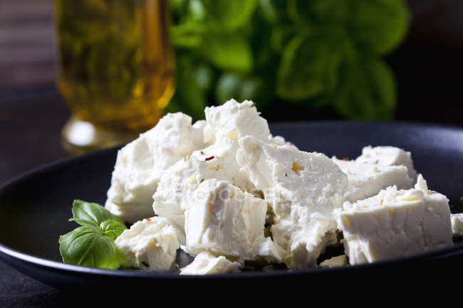Feta, erbe e foglie di basilico su piatto nero, primo piano — Foto stock