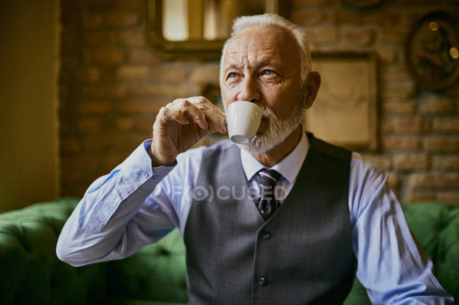 Элегантный пожилой мужчина пьет кофе в кафе — стоковое фото