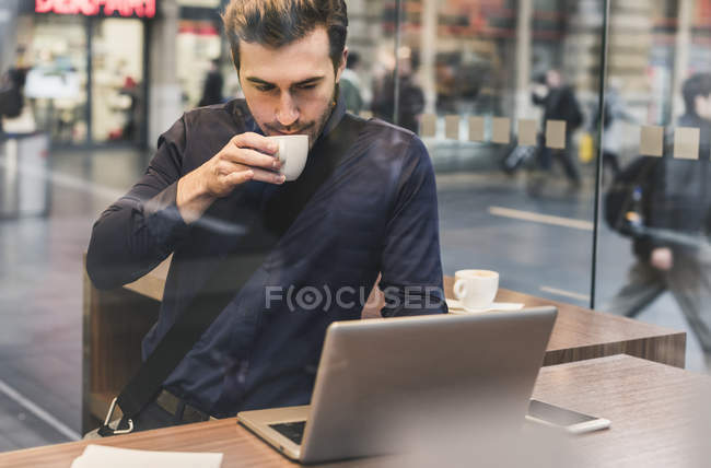 Joven hombre de negocios en un café en la estación de tren con taza de café y portátil - foto de stock