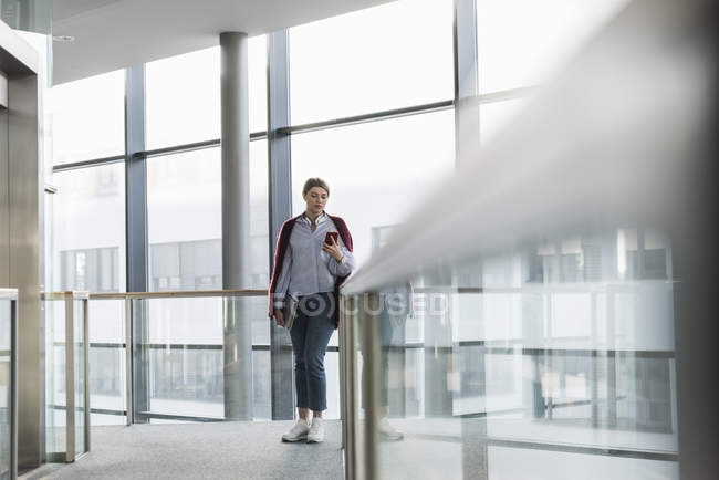 Young woman standing at the window and using cell phone — Stock Photo