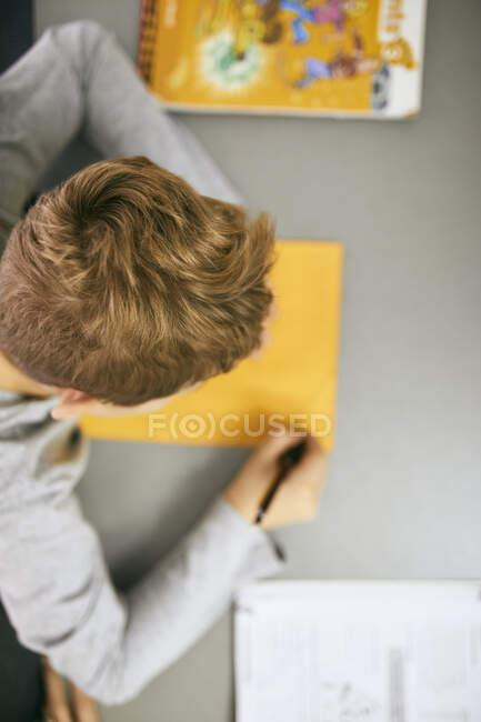 Colegial escribiendo en el escritorio en clase - foto de stock