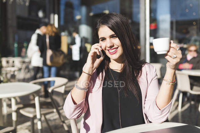 Souriant jeune femme d'affaires sur téléphone portable dans un café en plein air — Photo de stock