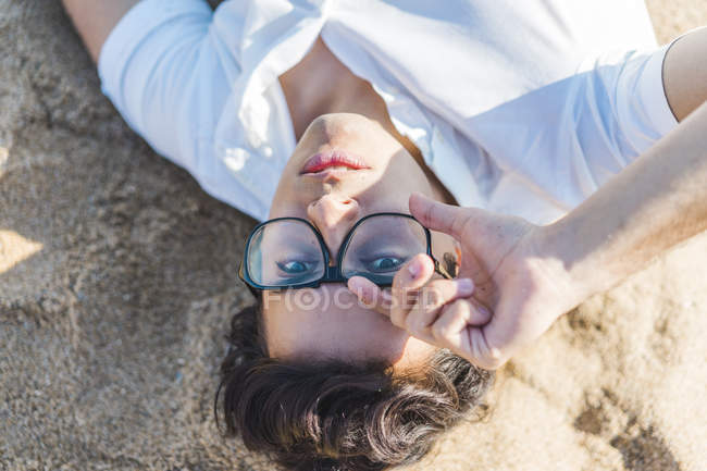 Портрет молодого человека в очках, лежащих в песке на пляже — стоковое фото