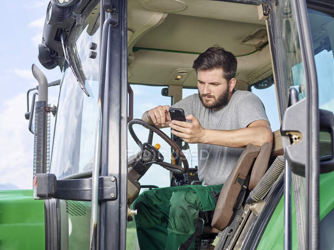 Фермер сидить на трактор і за допомогою мобільного телефону — стокове фото