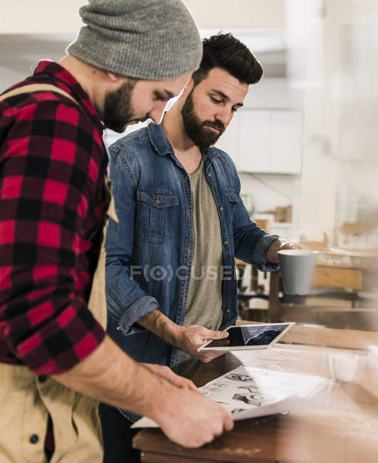 Deux hommes avec tablette regardant le brouillon en atelier — Photo de stock