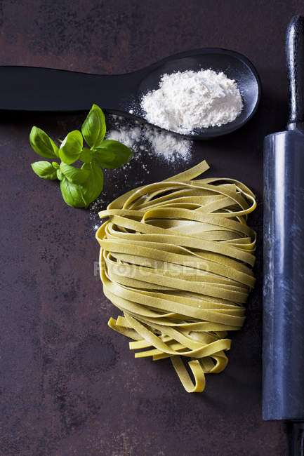 Green Tagliatelle, spoon of flour, basil leaves and rolling pin on rusty ground — Stock Photo