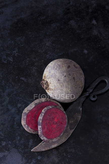 Whole and sliced beetroot and an old knife on dark metal — Stock Photo