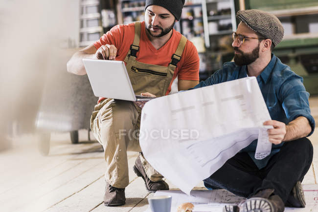 Deux hommes avec tablette regardant et projet assis sur le sol — Photo de stock