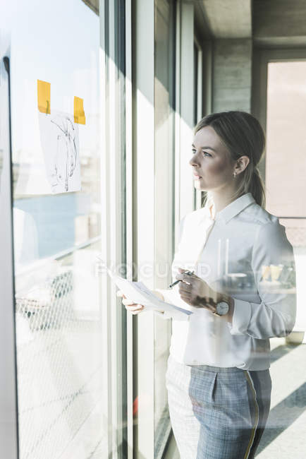 Jeune femme d'affaires regardant du papier à la fenêtre — Photo de stock