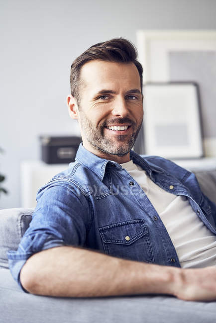 Retrato de homem sorridente sentado no sofá — Fotografia de Stock