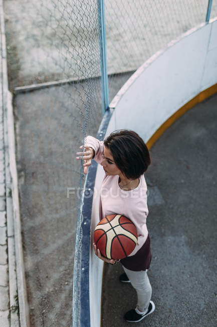 Молодая женщина, стоящая с баскетбольным мячом возле забора — стоковое фото