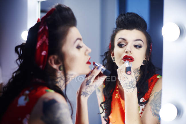 Image miroir de femme tatouée appliquant du rouge à lèvres rouge — Photo de stock