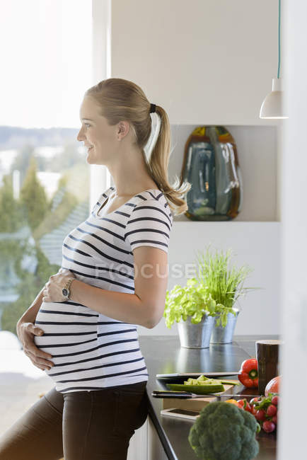 Smiling pregnant woman standing in kitchen at home — Stock Photo
