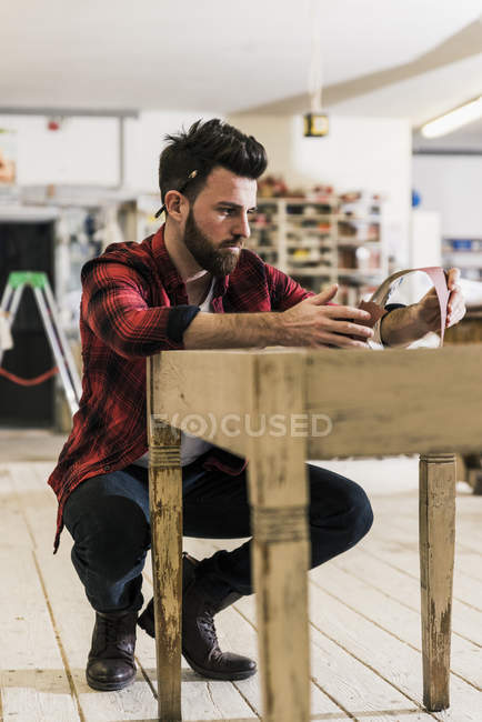 Uomo che tratta il legno in officina con carta vetrata — Foto stock