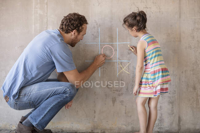 Father and daughter playing tic tac toe with chalk on a concrete wall — Stock Photo