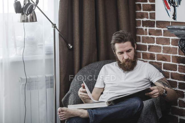 Uomo seduto sulla poltrona e guardando il libro del tavolino — Foto stock