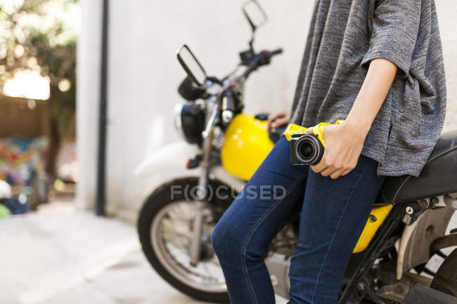 Gros plan de la femme avec caméra appuyée contre la moto — Photo de stock