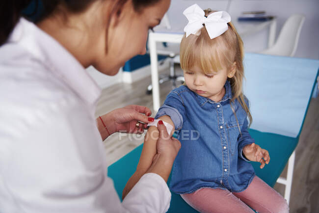 Médico aplicando tirita en el brazo de la niña en la práctica médica - foto de stock