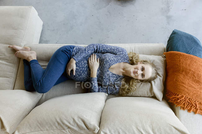 Ritratto di donna incinta sorridente sdraiata sul divano a casa — Foto stock