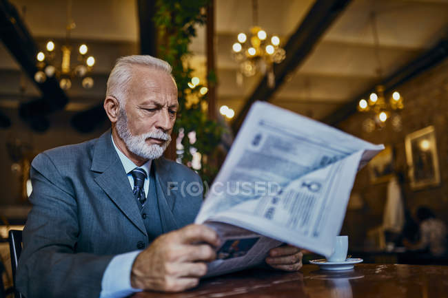 Елегантний старший чоловік читає газету в кафе — стокове фото