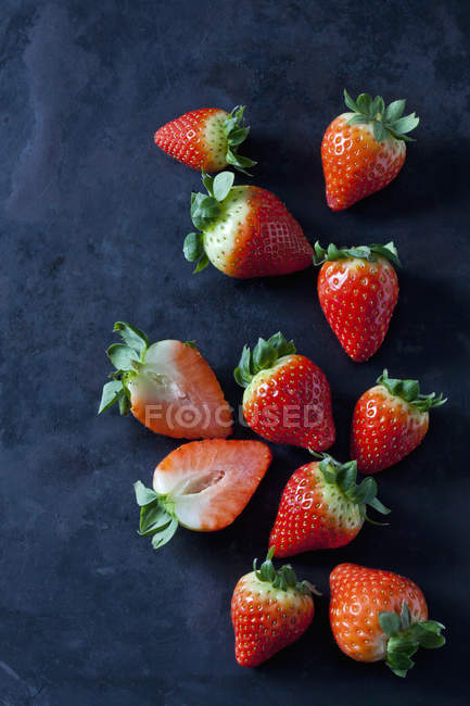 Fresh ripe whole and halved strawberries on dark grunge background — Stock Photo
