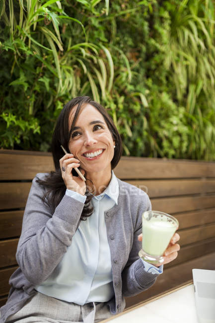 Усміхнена жінка на мобільному телефоні в садовому кафе — стокове фото