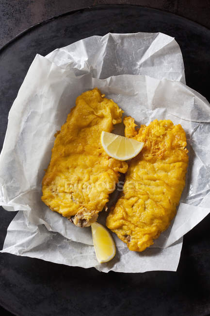 Fried coalfish filets and lemon slices on greaseproof paper — Stock Photo