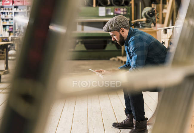 Mann sitzt in Werkstatt und benutzt Tablet — Stockfoto