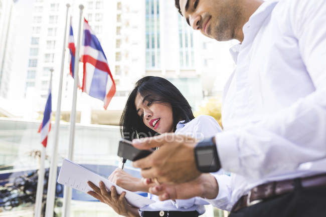 Thailand, Bangkok, businessman and businesswoman in the city with documents, cell phone and smartwatch — Stock Photo
