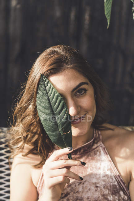 Porträt einer lächelnden jungen Frau, die Auge mit Blatt bedeckt — Stockfoto
