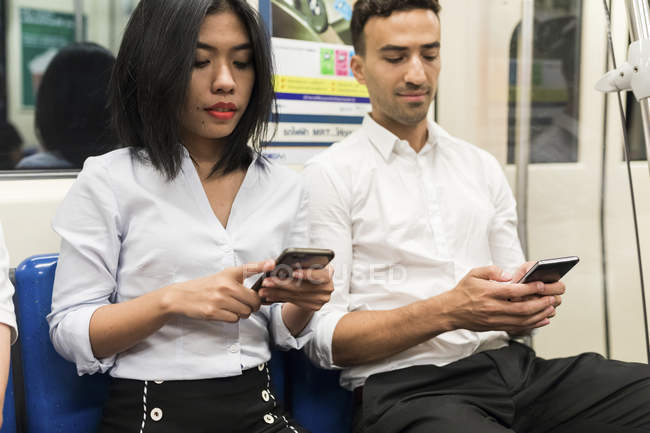 Homme d'affaires et femme d'affaires utilisant des téléphones portables dans le métro — Photo de stock
