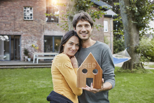 Retrato de casal sorridente no jardim de sua casa segurando modelo de casa — Fotografia de Stock