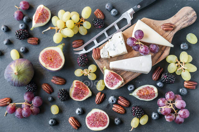 Assiette avec fromage, figues, raisins, bleuets, ronces, noix de pécan, planche à découper, couteau — Photo de stock