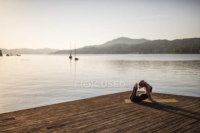 Mujer practicando yoga en embarcadero en el lago - foto de stock