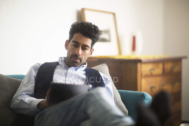 Portrait Of Relaxed Man Sitting On Couch At Home Using Tablet