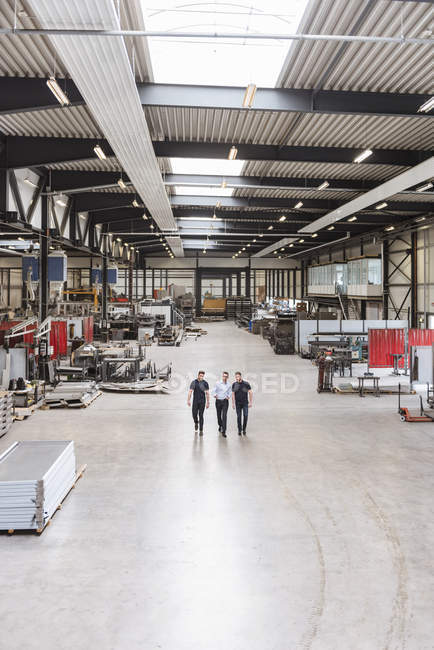 Three men walking and talking on factory shop floor — Stock Photo