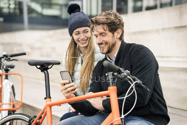 Casal sorridente com bicicletas e telefone celular na cidade — Fotografia de Stock