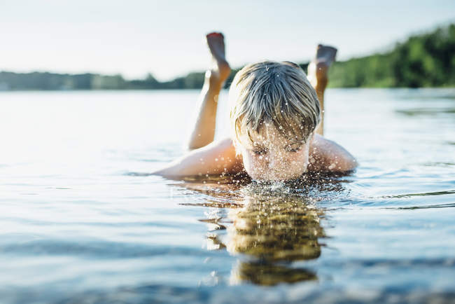 Boy in a lake blowing into water — Stock Photo
