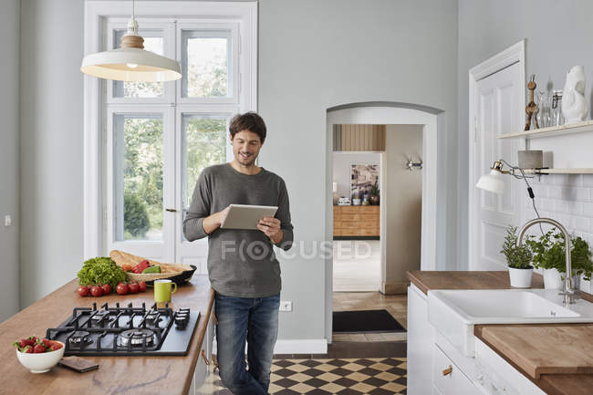 Hombre sonriente usando tableta en la cocina - foto de stock
