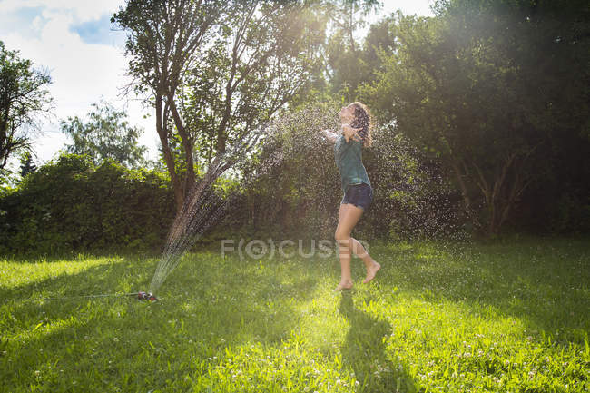 Fille s'amuser avec arroseur de pelouse dans le jardin — Photo de stock