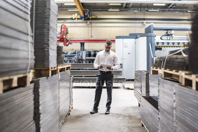 Homme d'affaires avec tablette debout sur le plancher de l'atelier de l'usine — Photo de stock