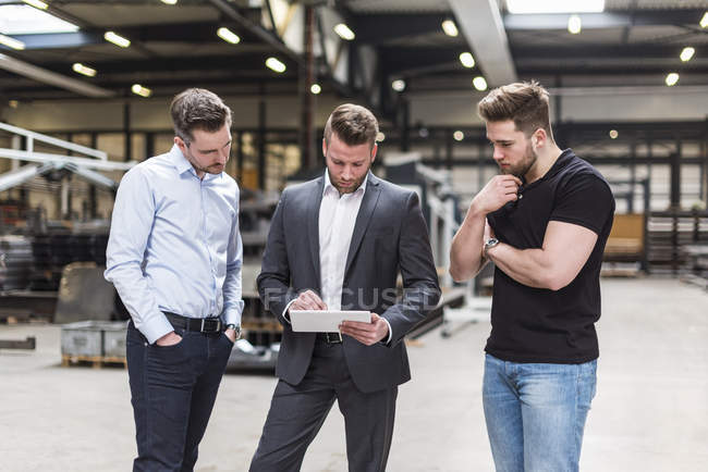 Three men sharing tablet on factory shop floor — Stock Photo
